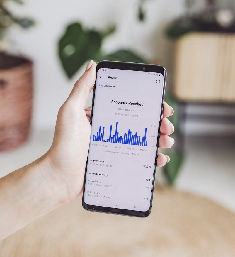 Mano con smartphone mostrando gráfico de alcance en redes sociales