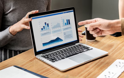 Personas analizando gráficos de datos en una computadora portátil en una reunión de trabajo.